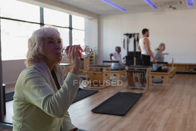 Senior woman drinking water in yoga center — Stock Photo