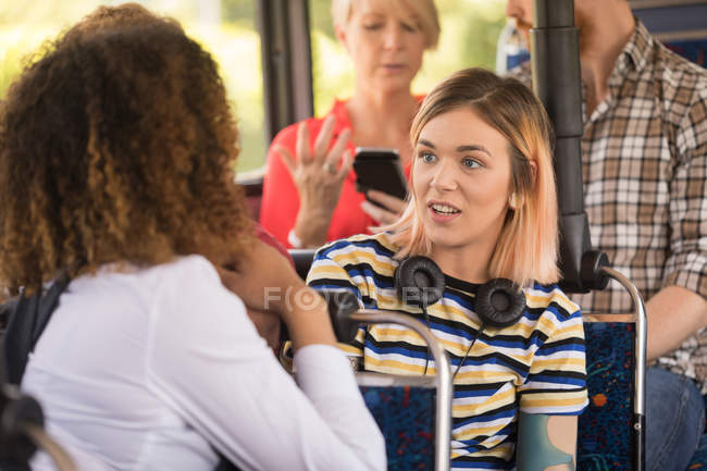 Female friends interacting while travelling in modern bus — Stock Photo