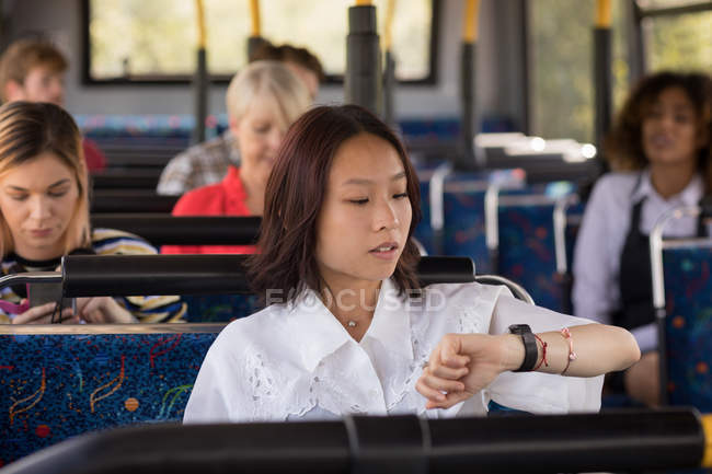 Feminino pendulares verificando o tempo enquanto viaja em ônibus moderno — Fotografia de Stock