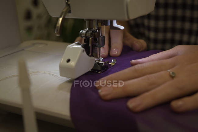 Primer plano del diseñador de moda utilizando la máquina de coser en el estudio de moda - foto de stock