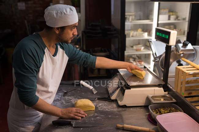 El panadero masculino que comprueba el peso de la masa en la panadería - foto de stock