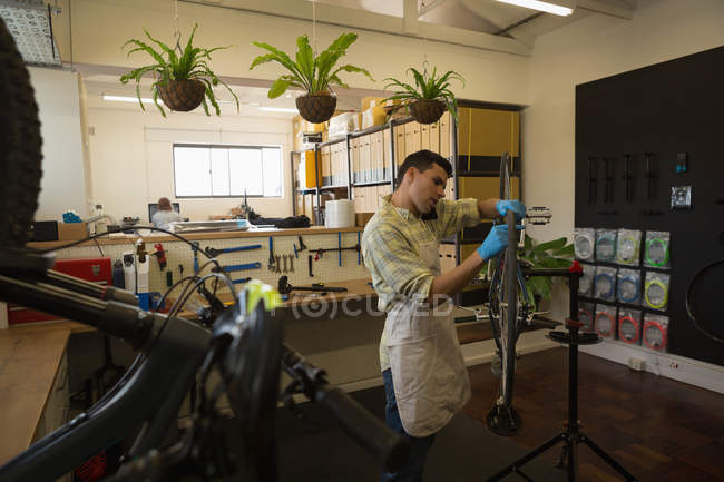 Hombre hablando en el teléfono móvil durante la reparación de la bicicleta en el taller - foto de stock