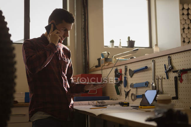Молодой механик разговаривает по мобильному телефону в мастерской — стоковое фото
