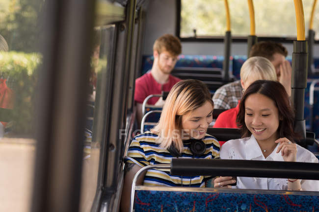 Подруги, пользующиеся мобильным телефоном во время путешествия на современном автобусе — стоковое фото