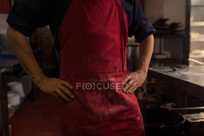 Padeiro masculino de pé com as mãos no quadril na padaria — Fotografia de Stock