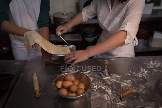 Sección media de panaderos con máquina para preparar pasta en panadería - foto de stock