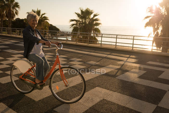 Senior woman riding bicycle at promenade on a sunny day — Stock Photo