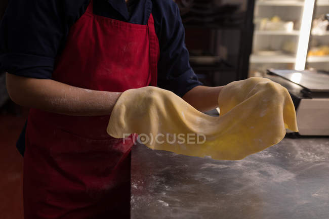 Panadero sosteniendo pasta hecha a mano en una panadería - foto de stock