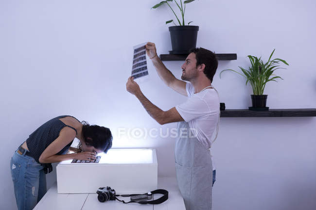Male photographer and female model looking at negative filmstrip in photo studio — Stock Photo