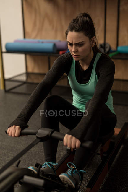 Young woman exercising on rowing machine in fitness studio — Stock Photo