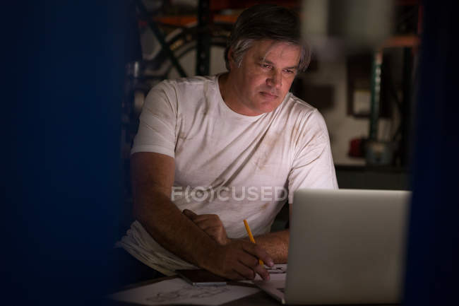 Mecánico masculino dibujar un modelo de coche mientras se utiliza el ordenador portátil en el garaje - foto de stock