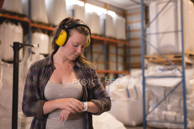 Trabalhadora feminina verificando o tempo no relógio inteligente no armazém — Fotografia de Stock
