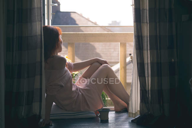 Mulher atenciosa olhando pela janela em casa — Fotografia de Stock