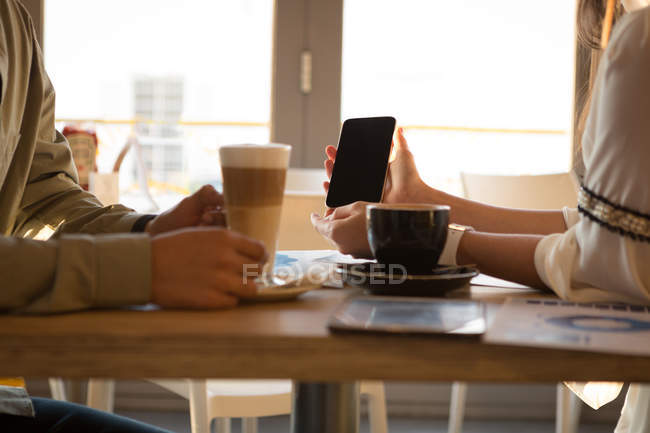 Sección media de la pareja discutiendo en el teléfono móvil en la cafetería - foto de stock