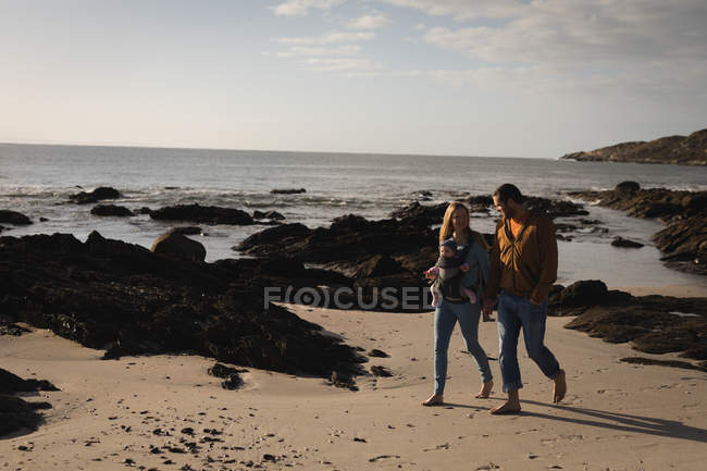 Родители с ребенком прогуливаются по пляжу в солнечный день — стоковое фото