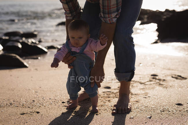 Close-up of father teaching baby to walk at beach — Stock Photo
