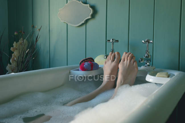 Sección baja de la mujer tomando baño en la bañera en el baño - foto de stock