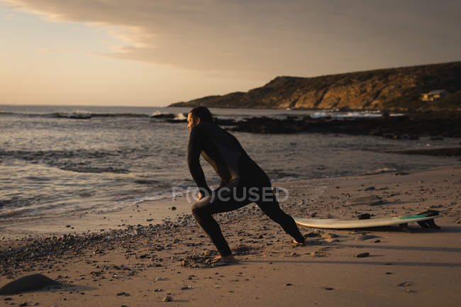 Surfista estirándose en la playa al atardecer - foto de stock