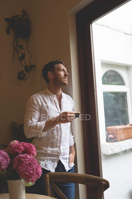 Homme réfléchi prenant un café tout en se tenant près de la fenêtre à la maison — Photo de stock