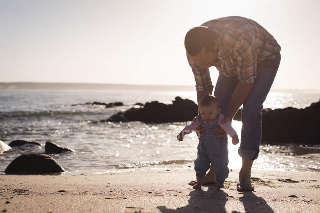 Отец учит ребенка ходить по пляжу в солнечный день — стоковое фото