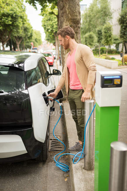 Hombre inteligente cargando coche eléctrico en la estación de carga - foto de stock