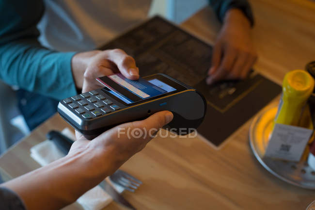 Primer plano del hombre que paga con tecnología NFC en la tarjeta de crédito en la cafetería - foto de stock