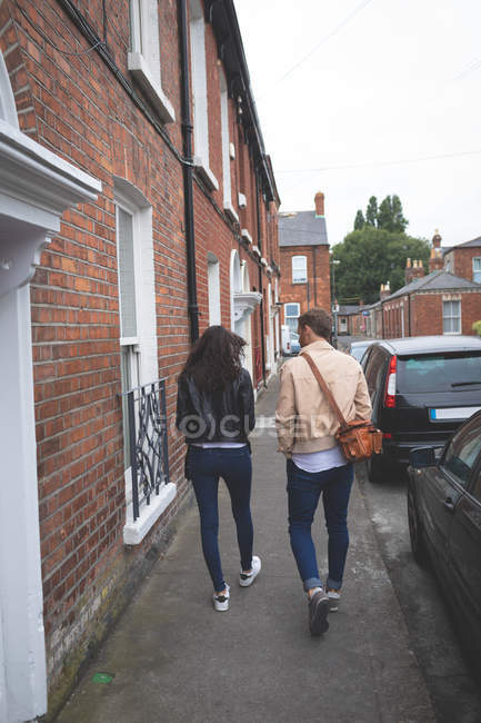 Vue arrière du couple marchant sur le trottoir de la ville — Photo de stock