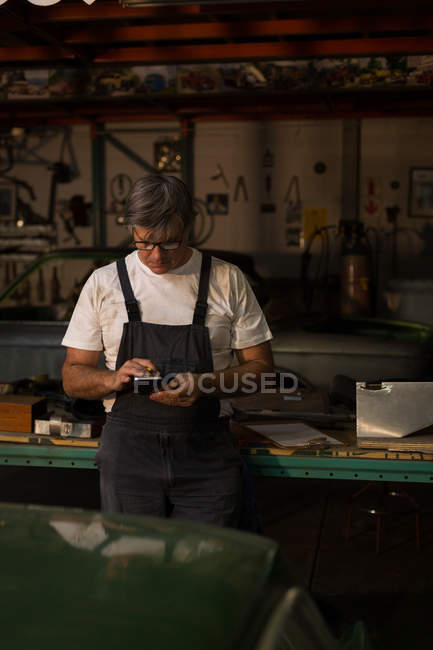 Mécanicien masculin utilisant le téléphone portable dans le garage — Photo de stock
