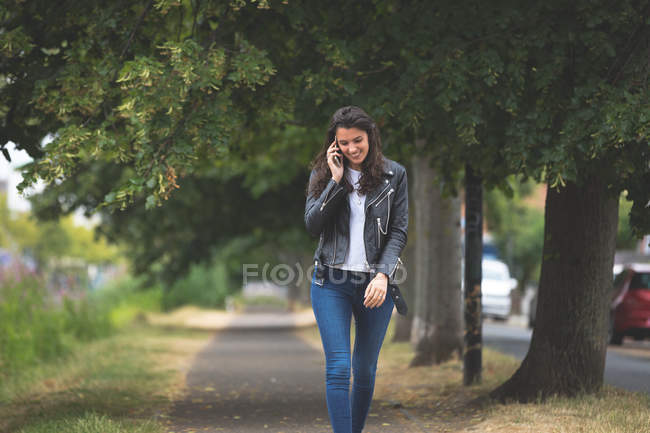 Beautiful woman talking on mobile mobile phone while walking in street — Stock Photo