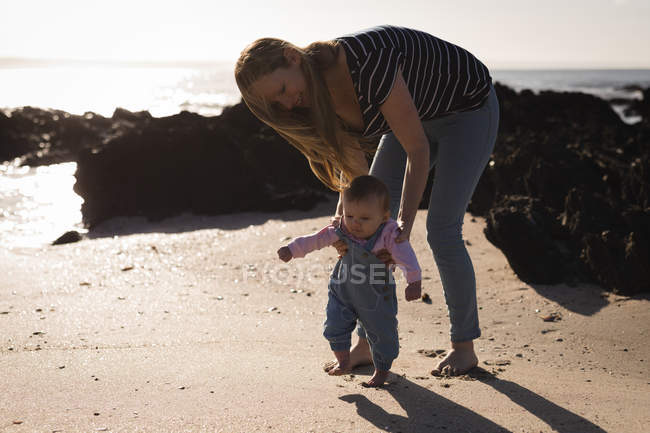 Мама учит ребенка ходить по пляжу в солнечный день — стоковое фото