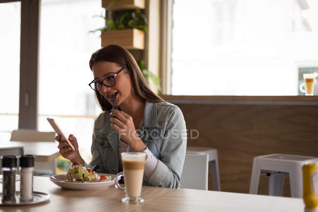 Frau benutzt Handy beim Essen im Café — Stockfoto