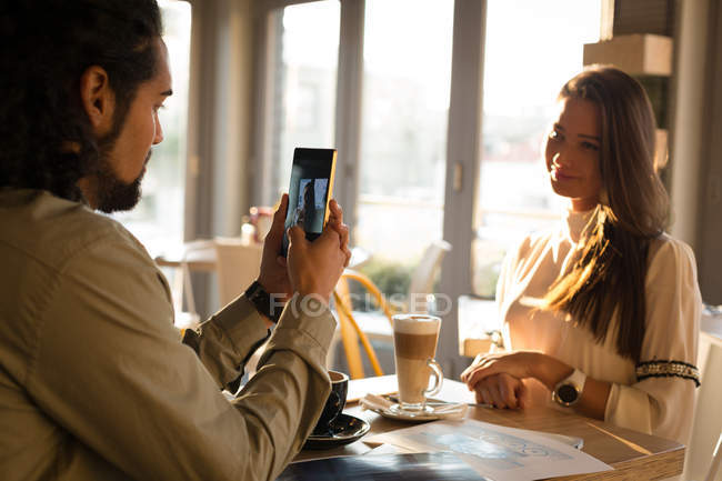 Мужчина фотографирует ее партнера в кафе — стоковое фото
