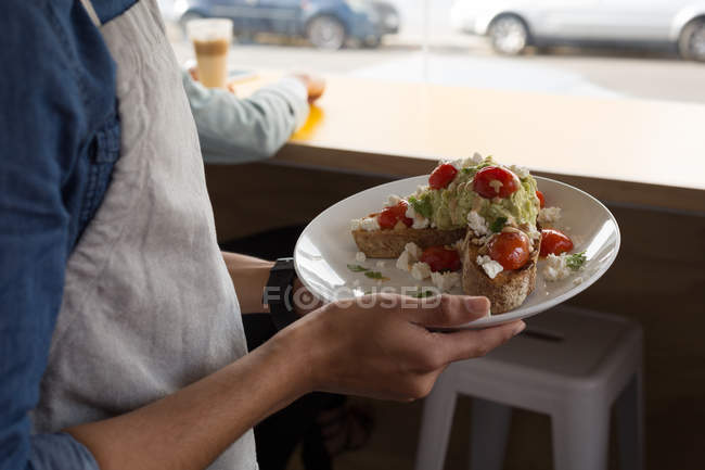 Primo piano di cameriere che tiene il piatto del cibo in caffè — Foto stock