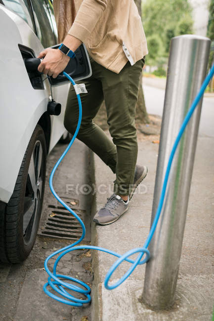 Низкая часть человека зарядки электрический автомобиль на зарядной станции — стоковое фото