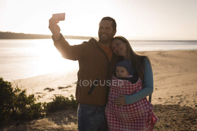 Щасливі батьки з дитиною беруть селфі на пляж — стокове фото