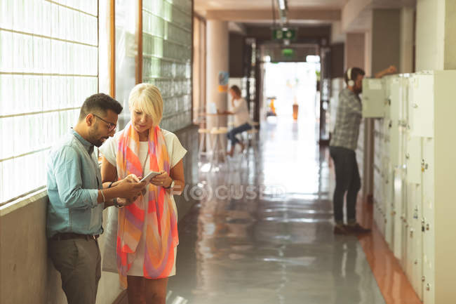 Руководители обсуждают цифровые планшеты в коридоре в офисе — стоковое фото