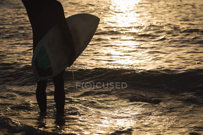 Baixa seção de surfista com prancha em pé na praia — Fotografia de Stock