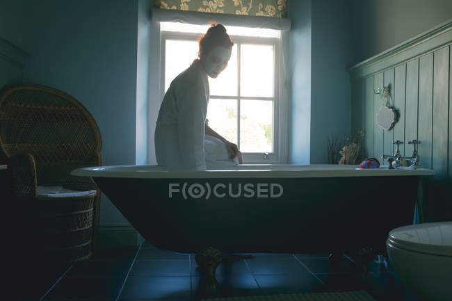 Mulher sentada na banheira verificando a água no banheiro em casa — Fotografia de Stock