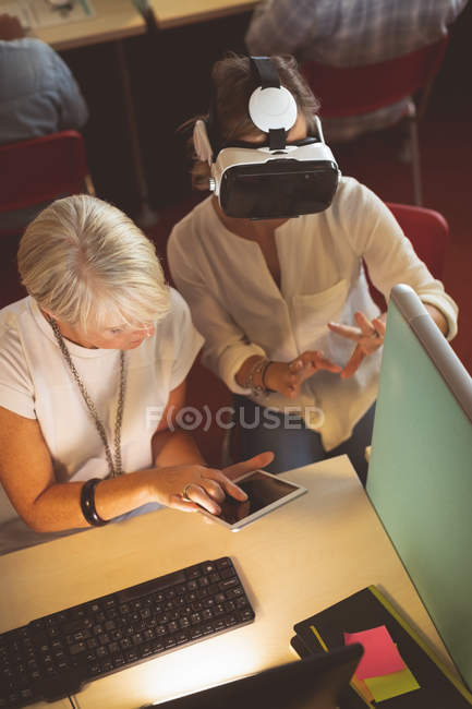 Высокоугольный вид женщин-руководителей, использующих гарнитуру виртуальной реальности и цифровой планшет за рабочим столом — стоковое фото