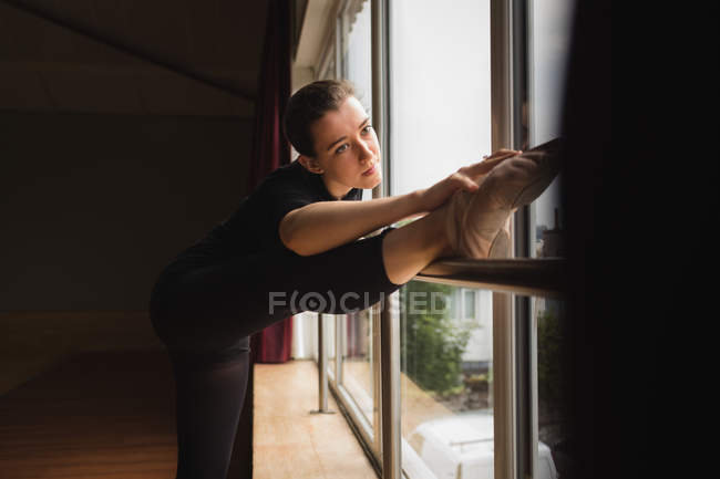 Bailarina estirándose mientras practica danza de ballet cerca de ventana en estudio de baile — Stock Photo