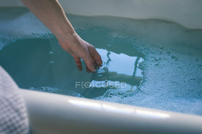 Primer plano de la mujer que revisa el agua en la bañera en el baño - foto de stock