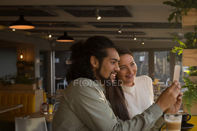 Улыбающаяся пара делает селфи в кафе — стоковое фото