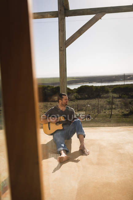 Молодий чоловік грає на гітарі в ганку пляжного будинку — стокове фото