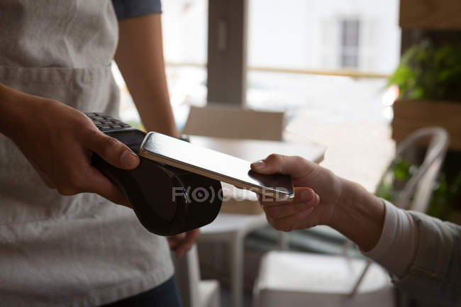 Primer plano de la mujer que paga con tecnología NFC en el teléfono móvil en la cafetería - foto de stock