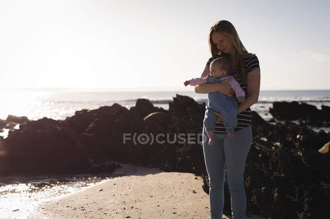 Mãe com bebê de pé na praia em um dia ensolarado — Fotografia de Stock