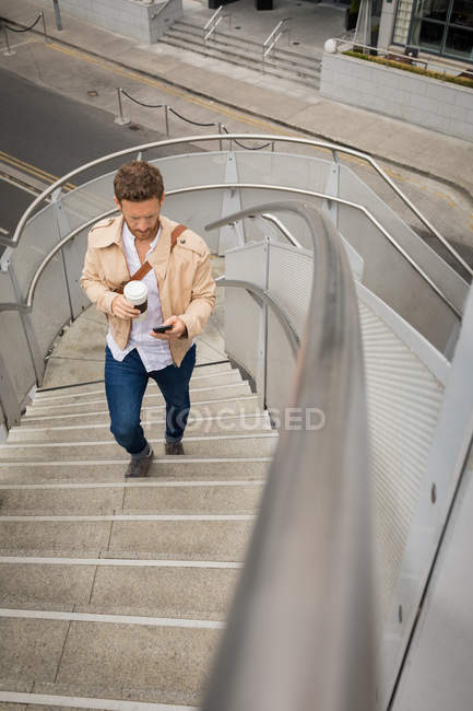 Hombre inteligente subiendo escaleras mientras usa el teléfono móvil - foto de stock