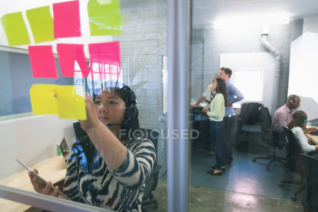 Female executive looking at sticky notes in office — Stock Photo