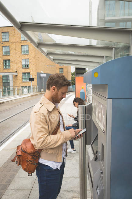 Вид сбоку на человека, пользующегося мобильным телефоном, стоя на платформе — стоковое фото