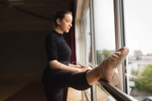 Ballerine s'étirant sur la barre tout en pratiquant la danse de ballet en studio de danse — Photo de stock