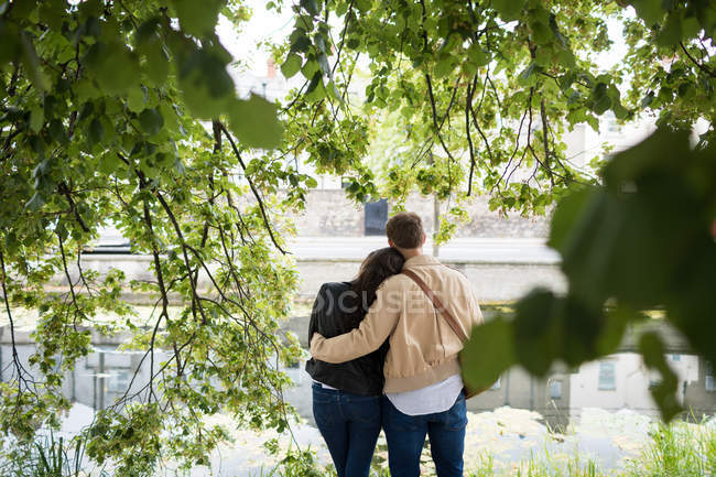Vista trasera de la pareja de pie cerca del lago - foto de stock